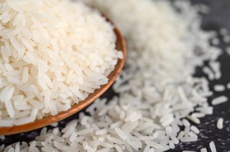 Milled rice in a bowl and a wooden spoon on the black cement floor. Selective focus